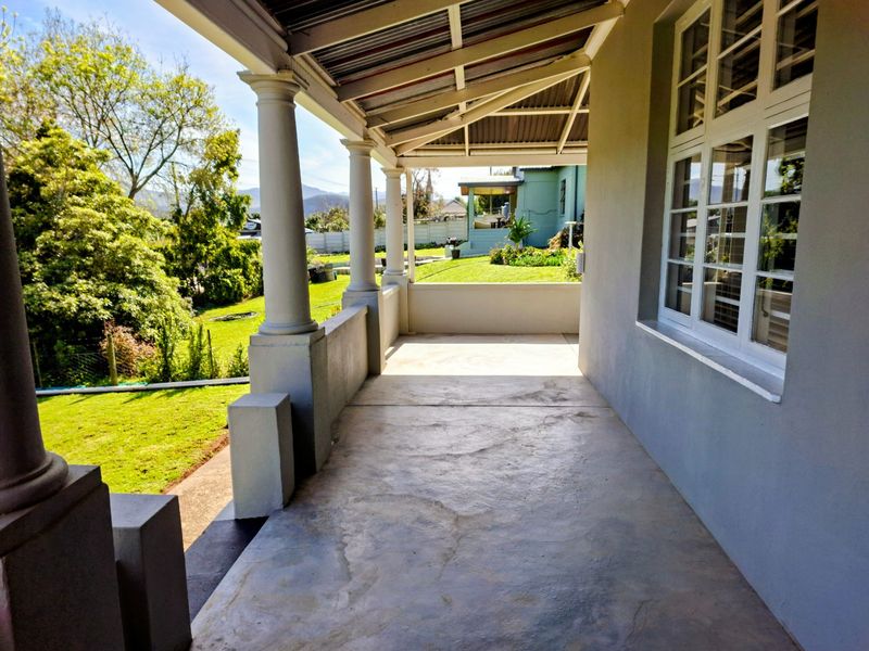A covered outdoor patio featuring concrete flooring, structural columns, and views of the surrounding garden area.