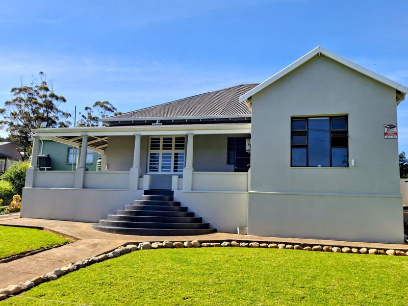A well-maintained single-story house featuring a covered front veranda, concrete entrance stairs, and a neat garden with stone edging.