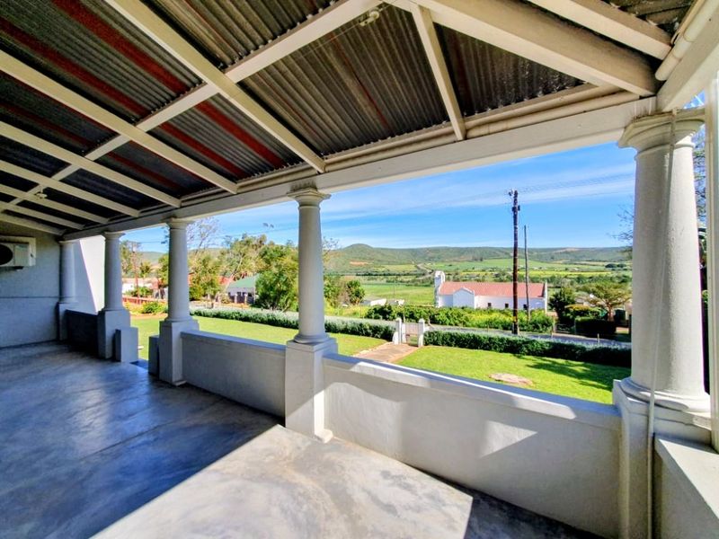 A spacious covered patio featuring concrete columns and flooring, offering expansive views of the surrounding landscape and countryside.