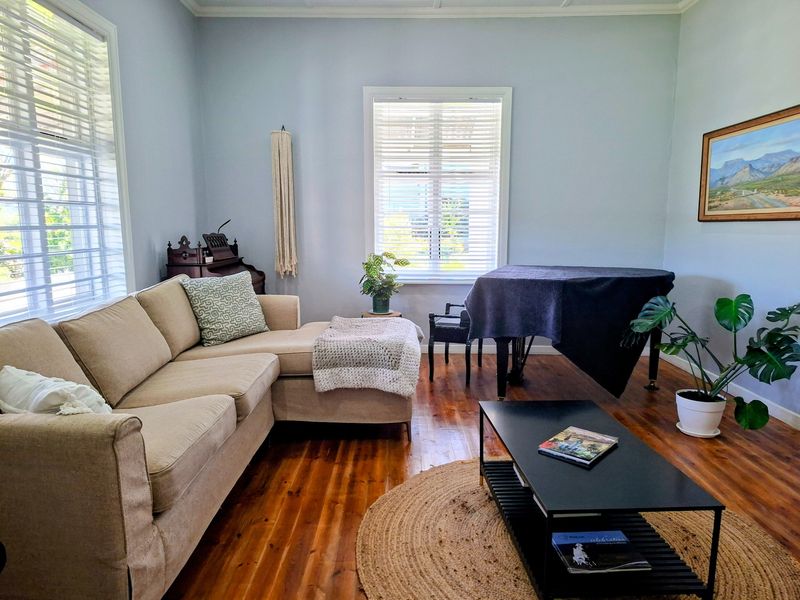 A bright and inviting living room featuring polished hardwood flooring, crown molding, and large windows fitted with venetian blinds.