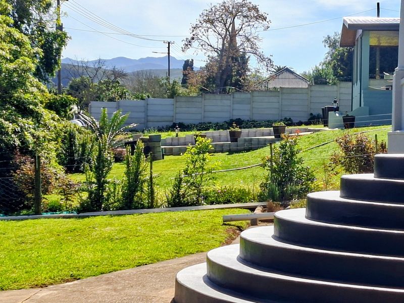 A view of the rear garden featuring a lawn, tiered retaining wall, and concrete steps leading from the house.