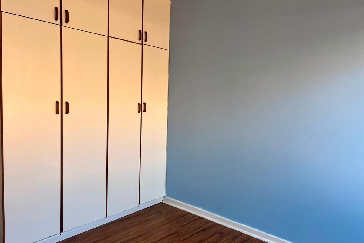 A clean, empty bedroom featuring light-colored built-in cupboards, blue painted walls, and dark wood-look laminate flooring.