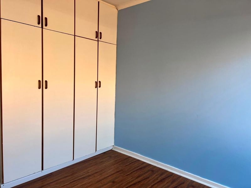 A clean, empty bedroom featuring light-colored built-in cupboards, blue painted walls, and dark wood-look laminate flooring.