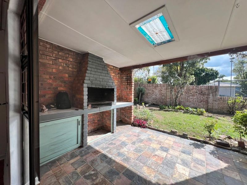 Covered patio area featuring a built-in brick braai, tiled flooring, and a skylight, overlooking a private garden with brick boundary walls.
