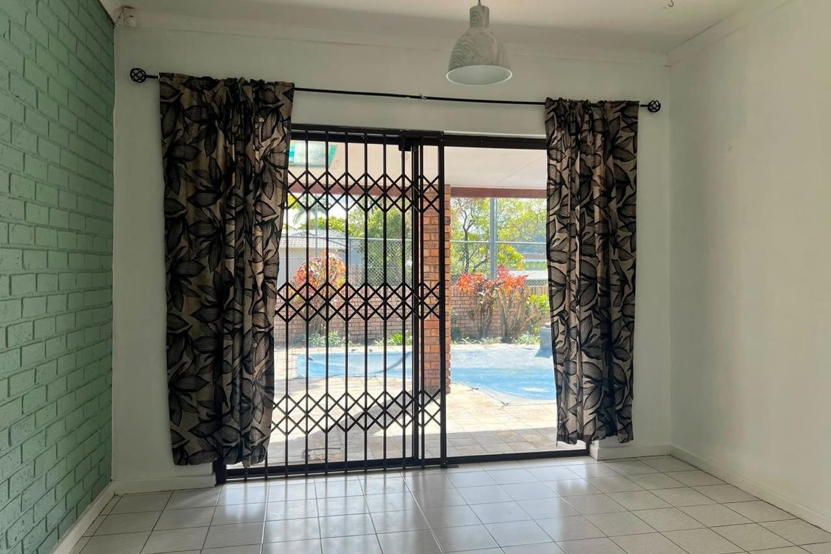 Bright living area featuring tiled floors, a painted brick accent wall, and sliding glass doors opening to a patio and pool area.