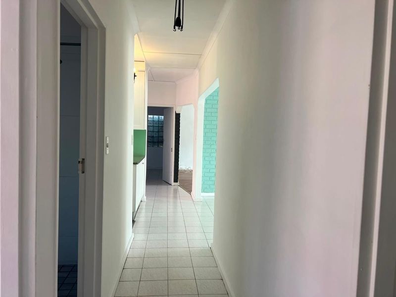 A bright, tiled hallway providing access to adjacent rooms, featuring a distinctive archway and a glass block window for natural light.