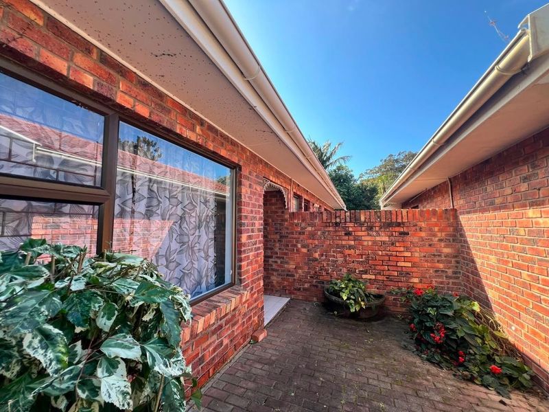 A private brick-paved rear courtyard area featuring exposed brick walls and established garden beds, providing a secluded outdoor space.