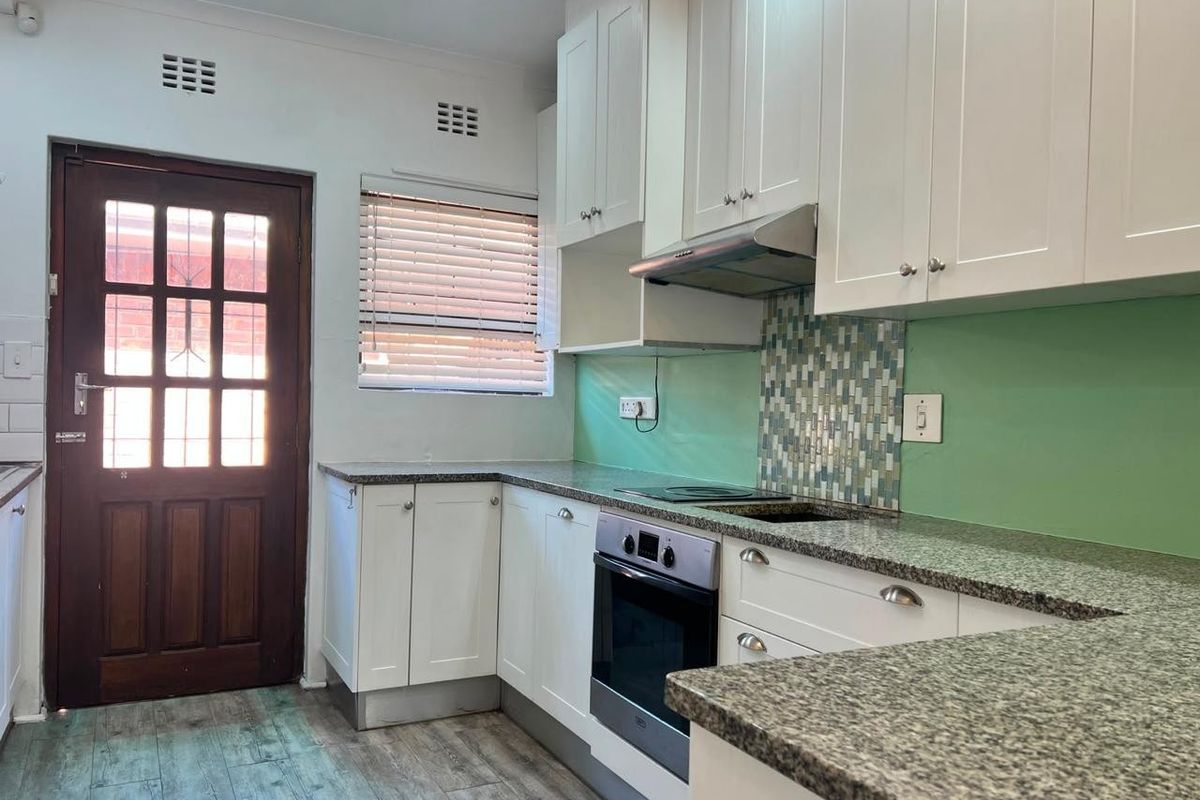 A clean, functional kitchen featuring white cabinetry, granite countertops, built-in oven, and a mosaic tile backsplash with direct access to the exterior.