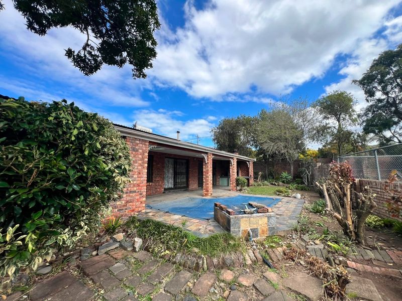 Rear exterior view featuring a brick facade, covered patio area, and a swimming pool with a cover, set within a garden with established landscaping.