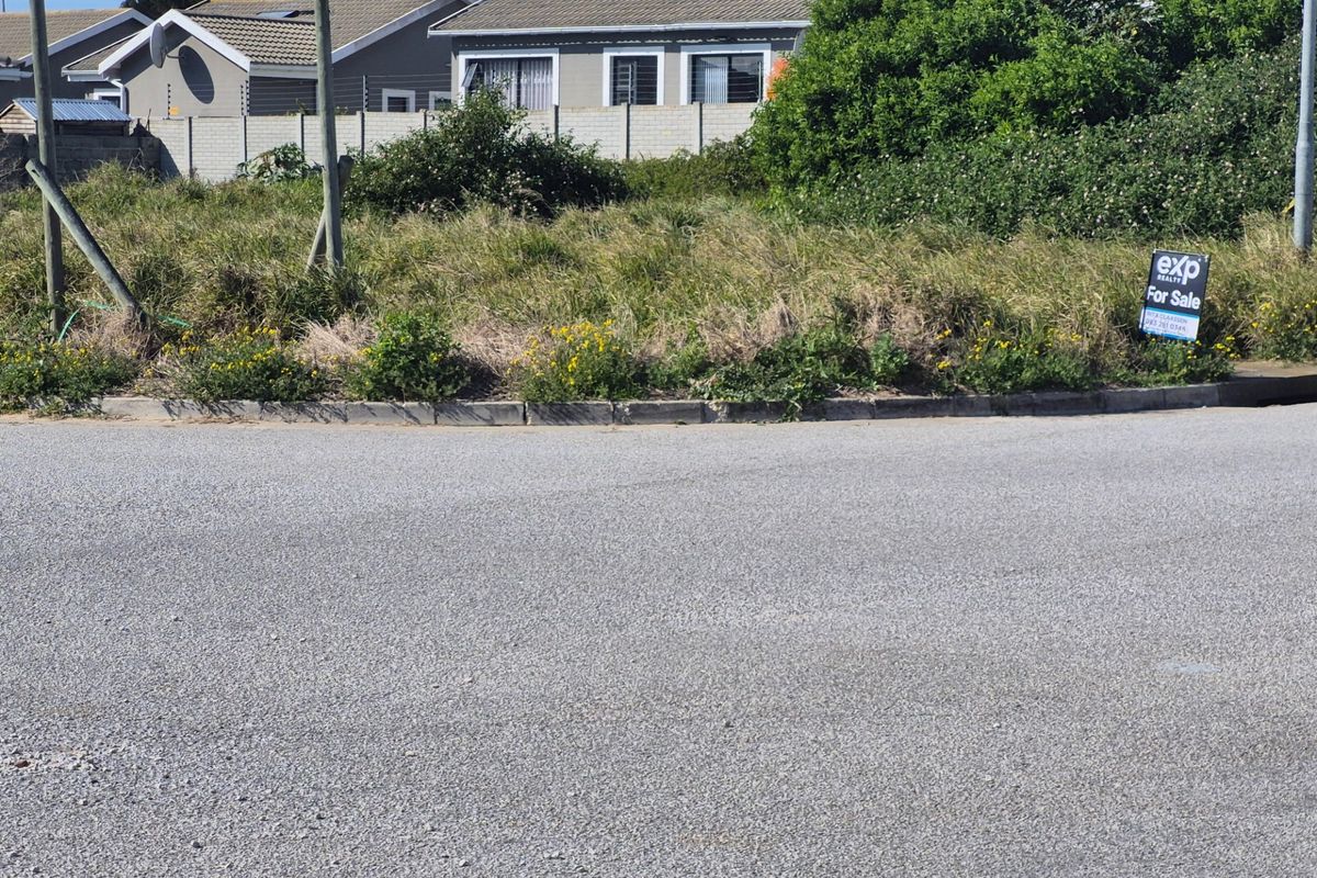 Street view of a vacant residential plot featuring asphalt road frontage and concrete kerbing, with a real estate for sale sign visible.