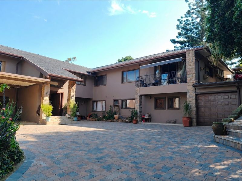 Spacious front exterior view of a multi-level house featuring stone cladding, a large paved driveway, a balcony, and an integrated garage.