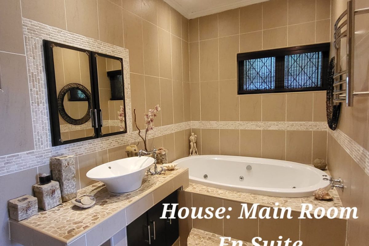 A well-appointed en-suite bathroom featuring a jetted bathtub, a vessel sink vanity, and neutral wall tiling with decorative mosaic accents.