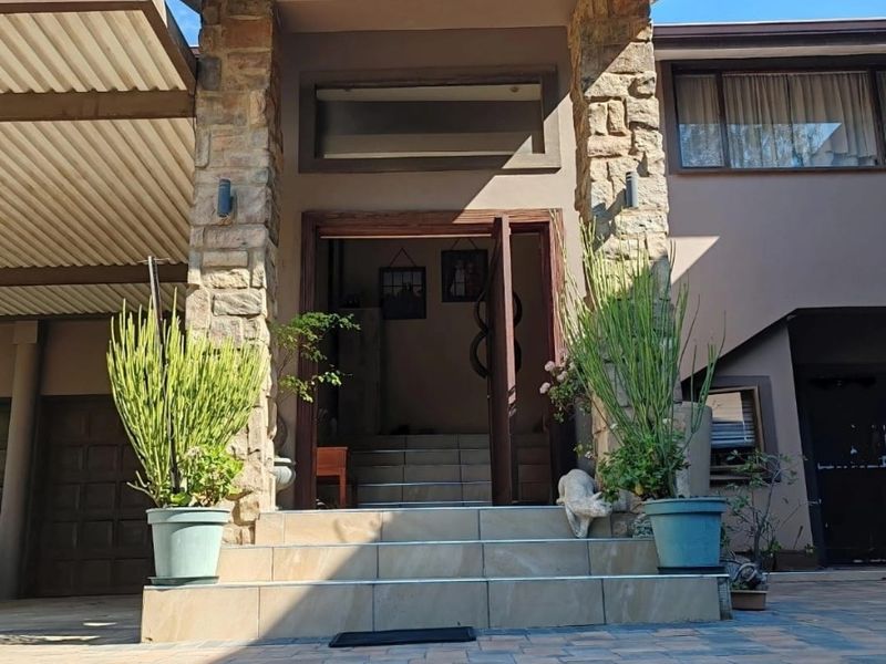 Front entrance of the house featuring stone cladding, tiled steps, and a paved driveway area with an adjacent carport.