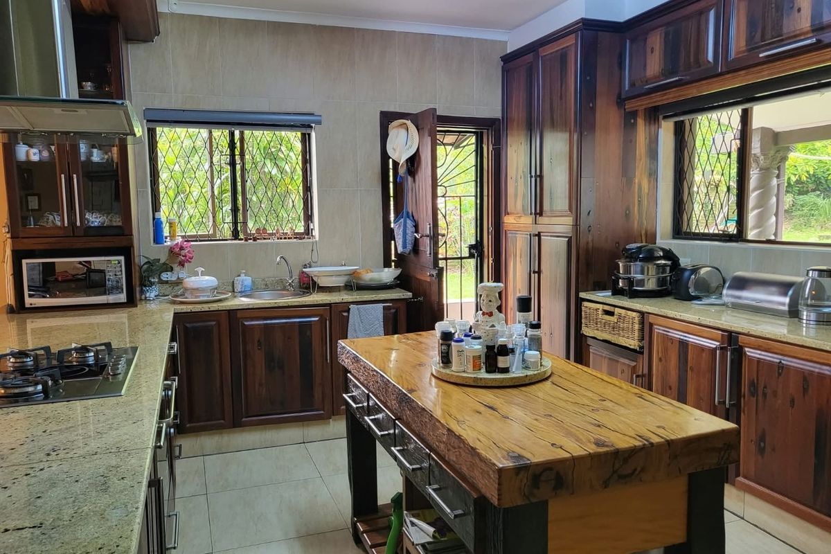A functional kitchen featuring dark wood cabinetry, granite countertops, a central wooden island, and a built-in gas hob with an extractor fan.