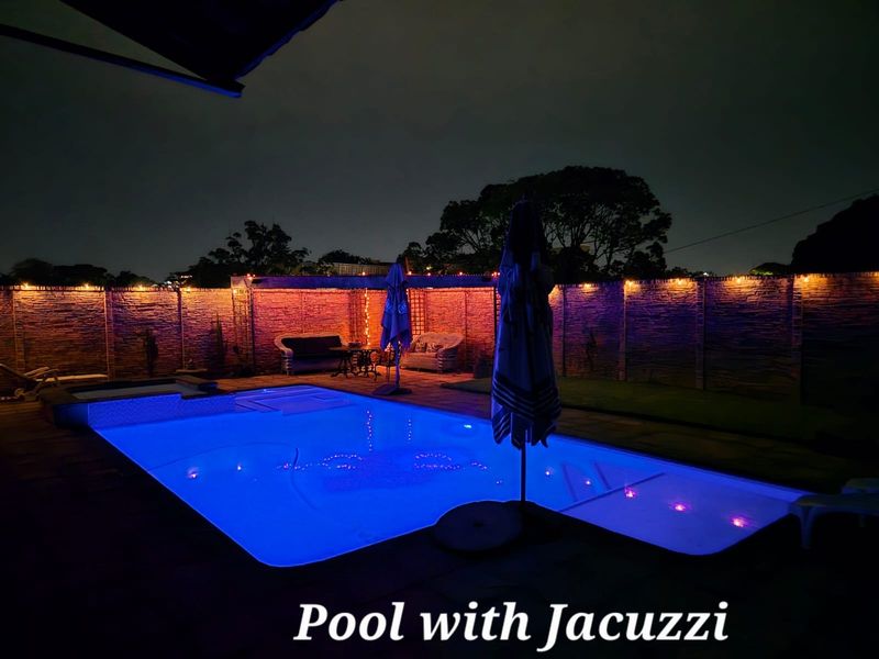 Night view of a backyard swimming pool featuring an integrated jacuzzi and surrounding paved patio area with boundary wall fencing.