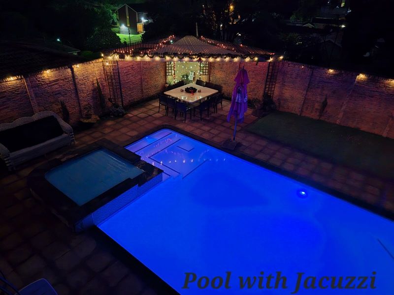 Nighttime aerial view of a backyard featuring a swimming pool, integrated jacuzzi, paved patio area, and a covered pergola.