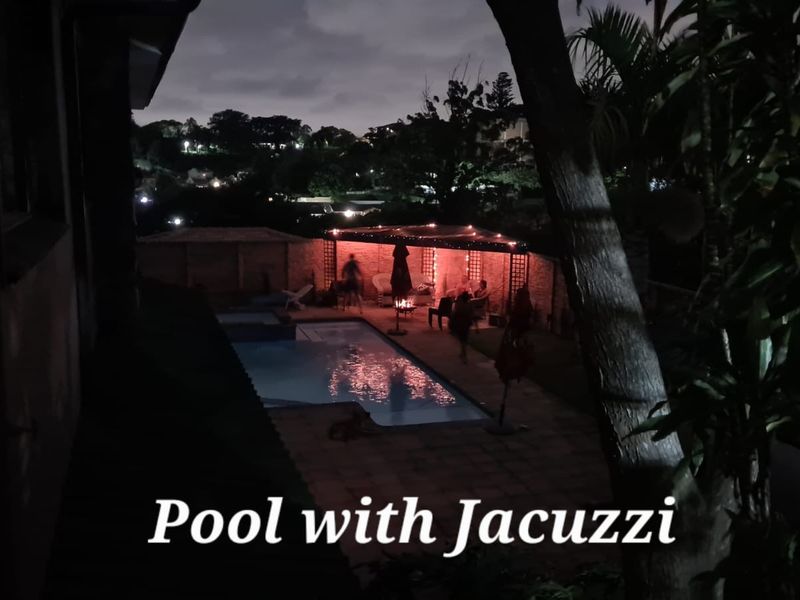 Night view of a backyard swimming pool area featuring a built-in jacuzzi and a covered pergola entertainment space.