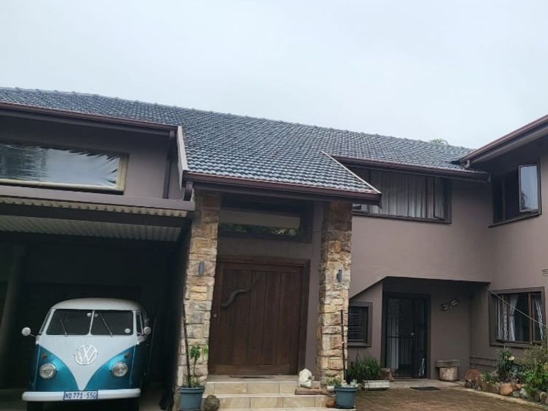 Front elevation of a multi-story house featuring stone cladding accents, a timber entrance door, tiled roof, and a paved driveway with an integrated carport.