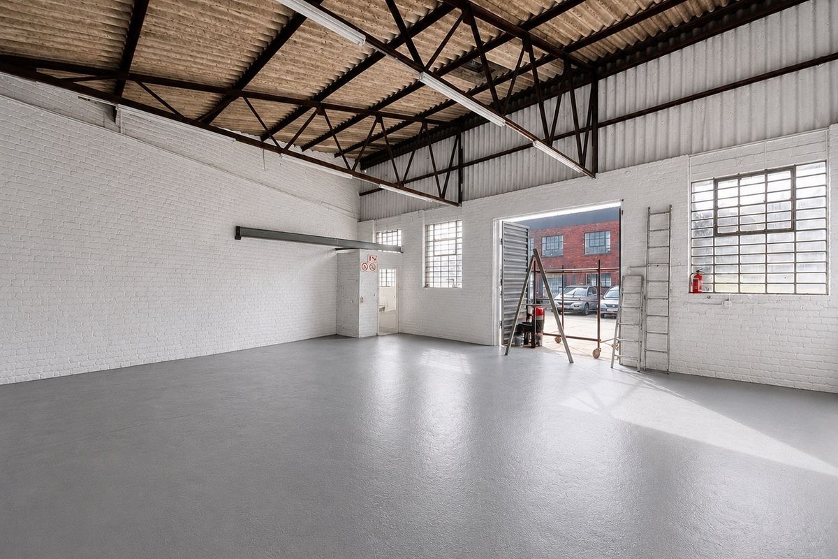 Spacious industrial warehouse unit featuring high ceilings with exposed steel trusses, painted brick walls, durable epoxy flooring, and large roller shutter access.