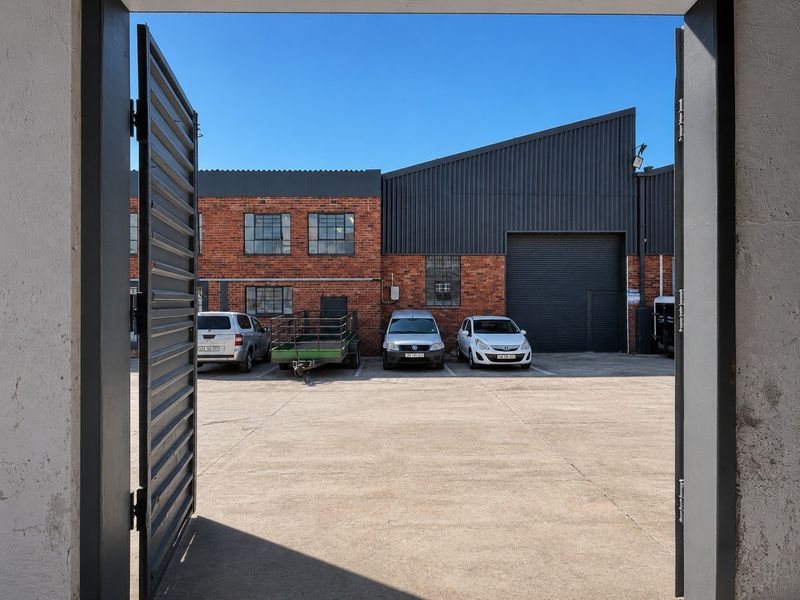 View of an industrial yard featuring a concrete surface, exposed brick building facade, and a large roller shutter door for vehicle access.
