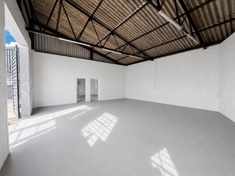 Spacious industrial utility space featuring high ceilings with exposed steel trusses, painted brick walls, and a clean epoxy-coated concrete floor.