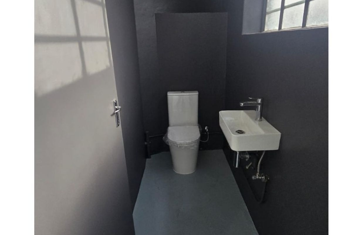 A modern, minimalist industrial-style bathroom featuring a wall-mounted basin, chrome fixtures, and a clean, dark-painted interior with a large steel-framed window.