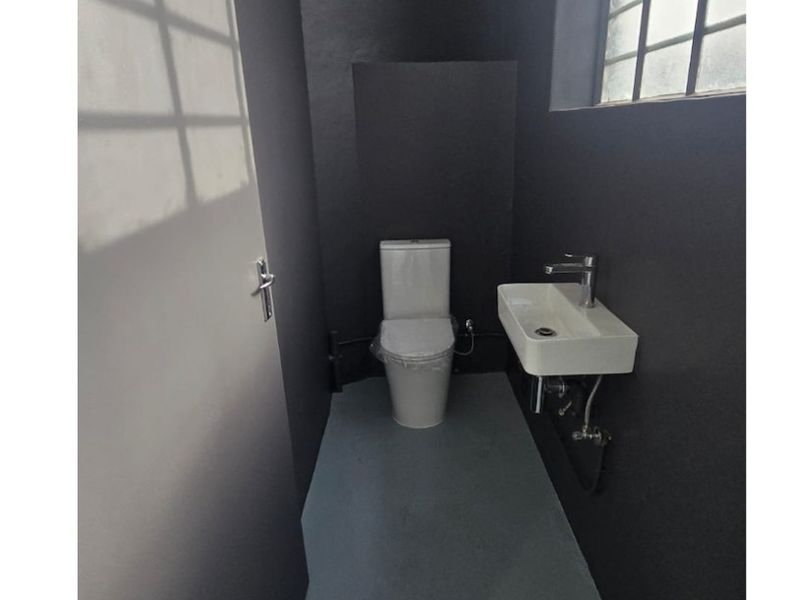 A modern, minimalist industrial-style bathroom featuring a wall-mounted basin, chrome fixtures, and a clean, dark-painted interior with a large steel-framed window.