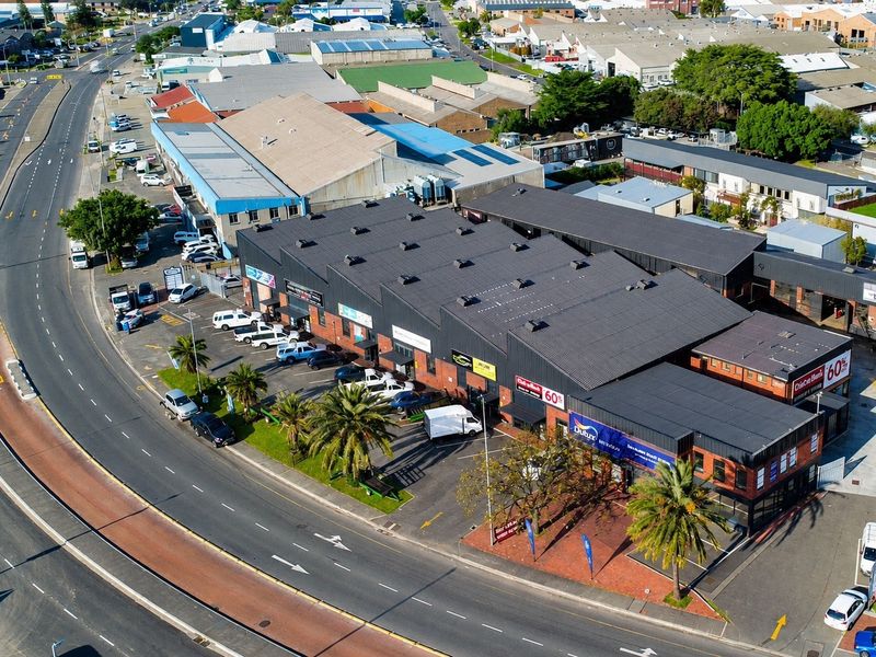 Aerial view of a commercial industrial complex featuring a large metal roof, brick facade, and dedicated asphalt parking area.
