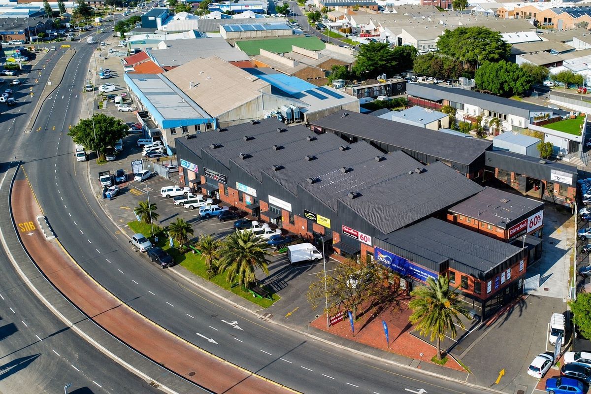 Aerial view of a commercial industrial complex featuring a large metal roof, brick facade, and dedicated asphalt parking area.