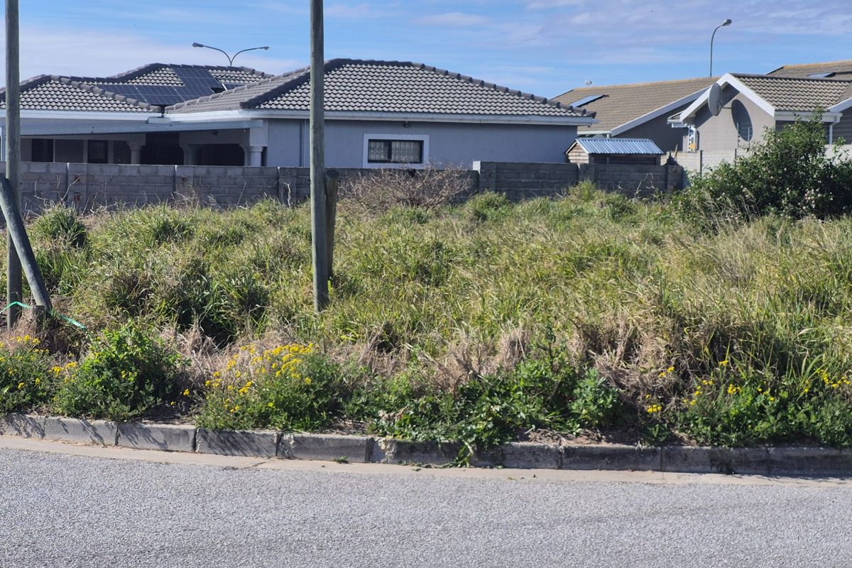 A vacant residential plot featuring concrete kerbing and a boundary wall, currently covered in overgrown vegetation.