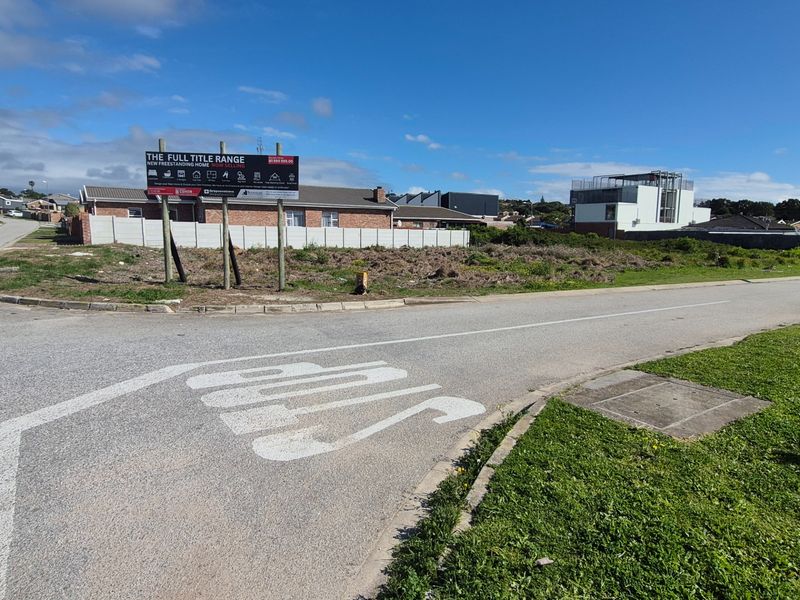 A vacant residential plot situated on a corner lot, featuring street access and surrounding neighborhood development.