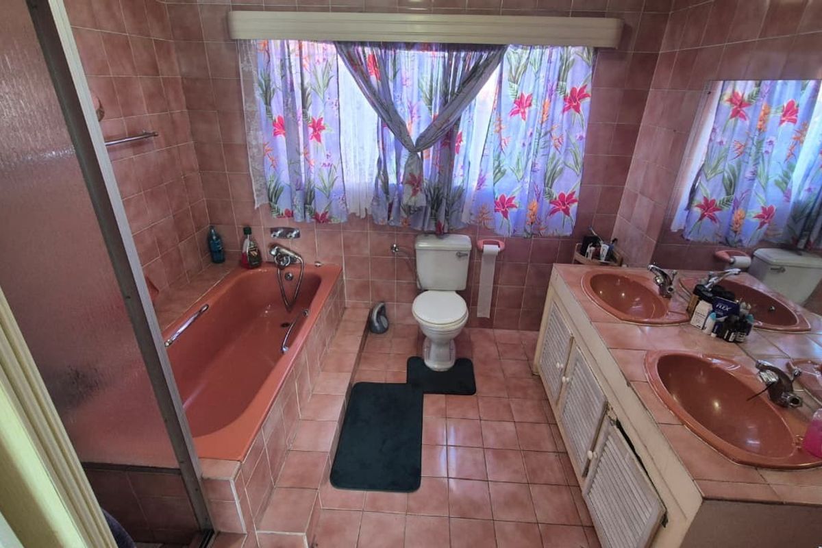 A dated bathroom featuring a double vanity, bathtub, and toilet with original pink tiling throughout.