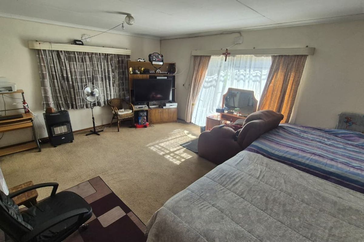A spacious bedroom featuring carpet flooring and large windows with curtain rails, offering potential for modernization and aesthetic updates.