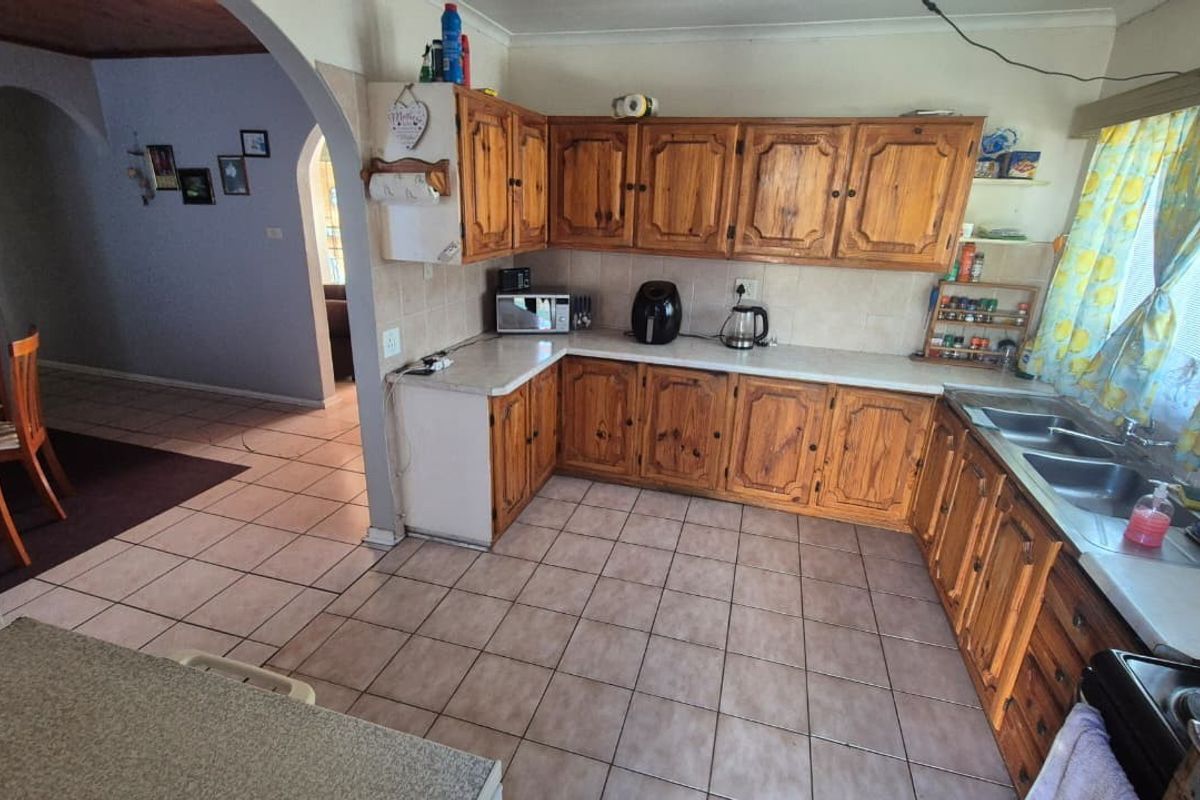 A functional kitchen featuring traditional wooden cabinetry, laminate countertops, a double stainless steel sink, and tiled flooring, offering potential for modern updates.