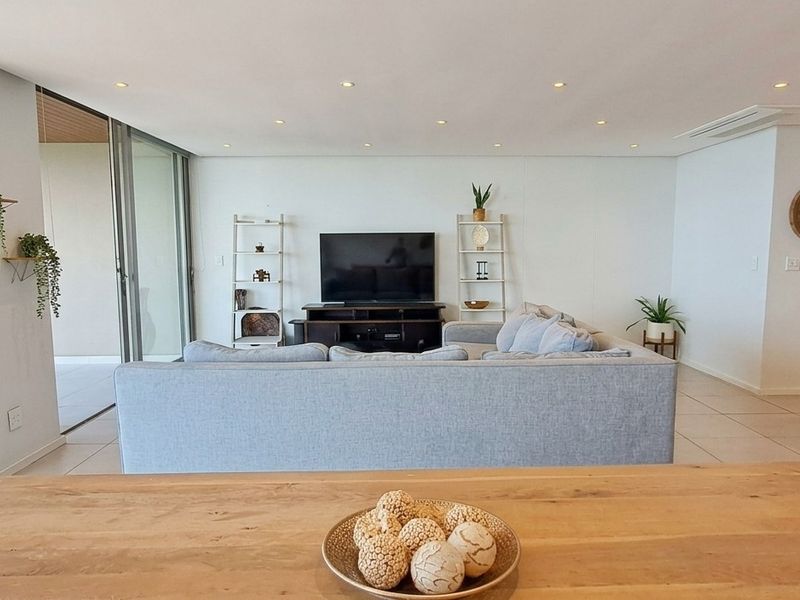 Spacious open-plan living area featuring tiled floors, recessed lighting, and large sliding glass doors leading to a balcony with ocean views.