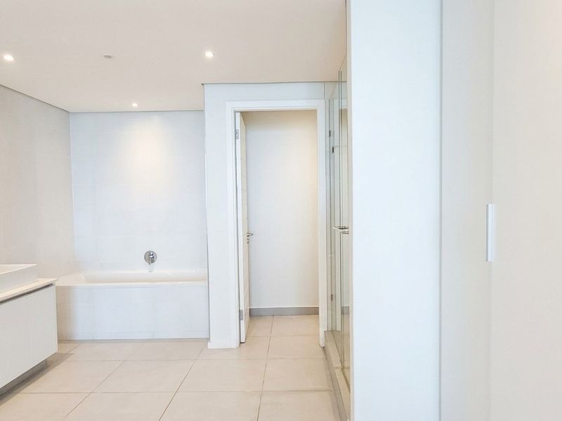 A modern, minimalist bathroom featuring a double vanity, a built-in bathtub, and a separate glass-enclosed shower with clean white finishes.