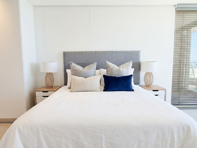 Modern bedroom featuring built-in cupboards, neutral tiled flooring, and a large sliding glass door providing natural light and access to the balcony.