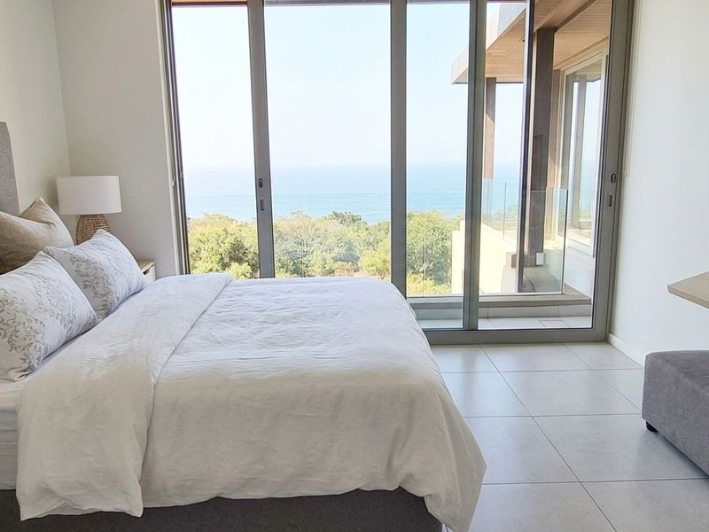 Modern bedroom featuring floor-to-ceiling sliding glass doors that open to a balcony with scenic ocean views and tiled flooring throughout.