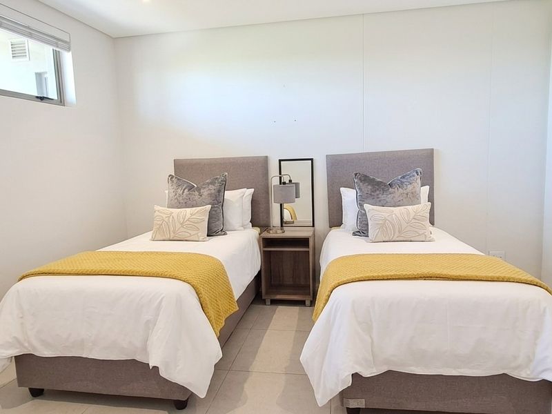 A bright and modern bedroom featuring neutral tiled flooring, built-in cupboards, and a high-level window providing natural light.