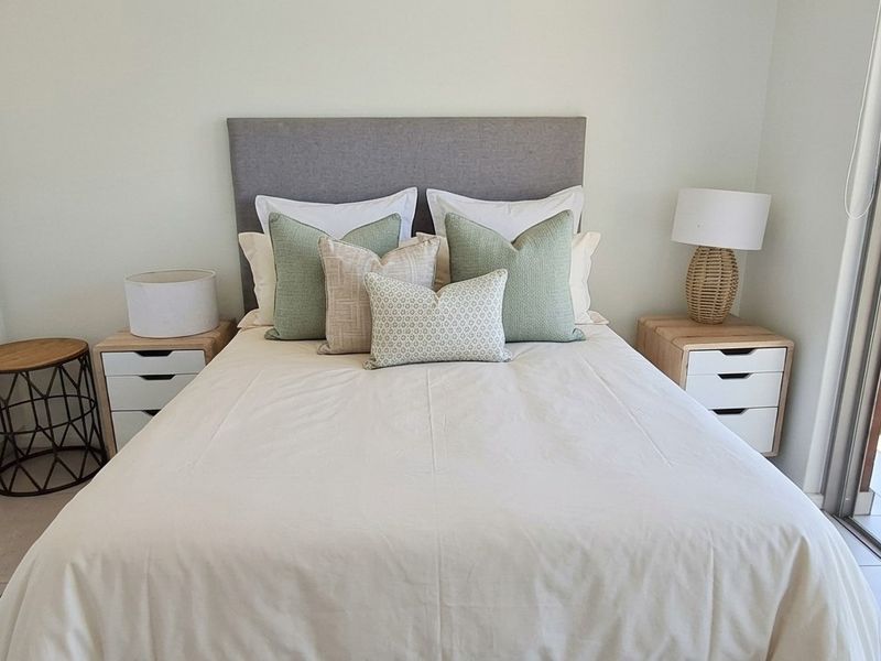 A bright, modern bedroom featuring built-in cupboards, tiled flooring, and a large sliding glass door providing access to an outdoor balcony.