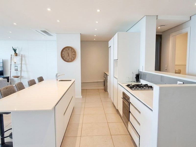 Modern open-plan kitchen and living area featuring a central island, built-in appliances, sleek cabinetry, and recessed lighting in a bright, contemporary penthouse setting.