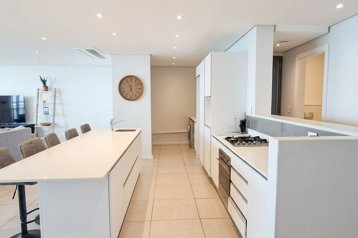 Modern open-plan kitchen and living area featuring a central island, built-in appliances, sleek cabinetry, and recessed lighting in a bright, contemporary penthouse setting.