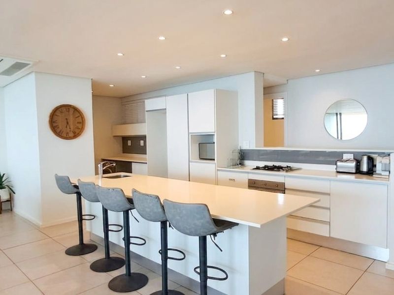Modern open-plan kitchen featuring a central island with stone countertops, built-in gas hob, oven, and sleek cabinetry, complemented by recessed lighting and tiled floors.