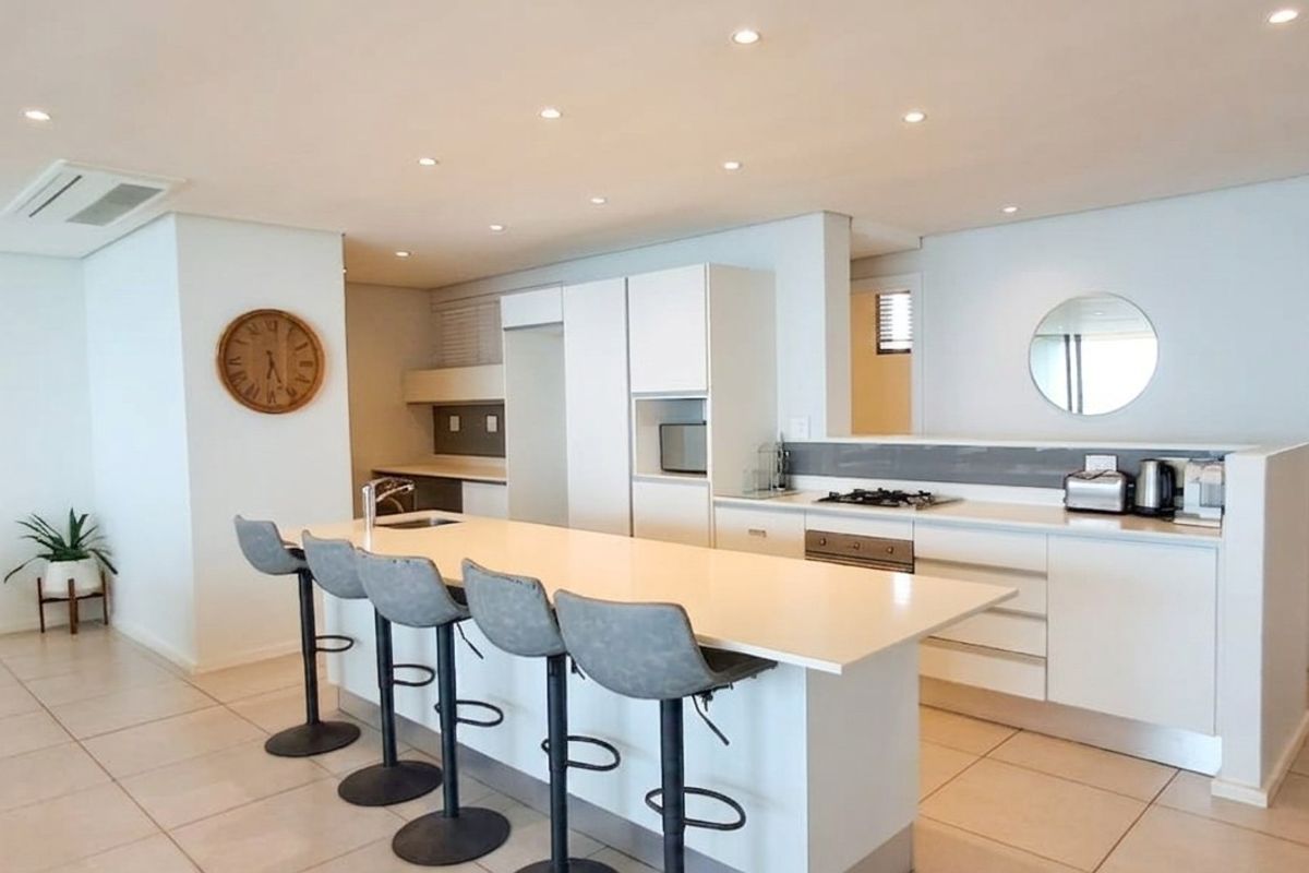 Modern open-plan kitchen featuring a central island with stone countertops, built-in gas hob, oven, and sleek cabinetry, complemented by recessed lighting and tiled floors.
