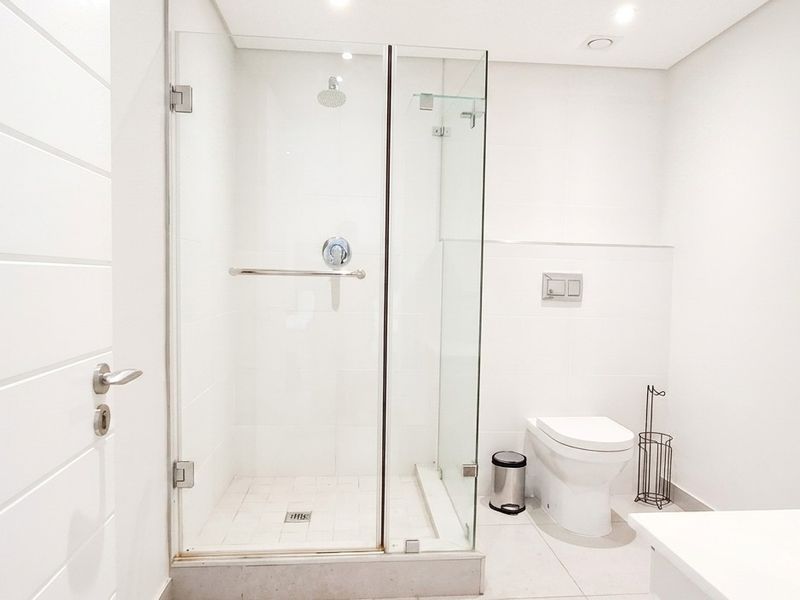 A modern, minimalist bathroom featuring a glass-enclosed shower, wall-mounted toilet with concealed cistern, and clean white finishes throughout.