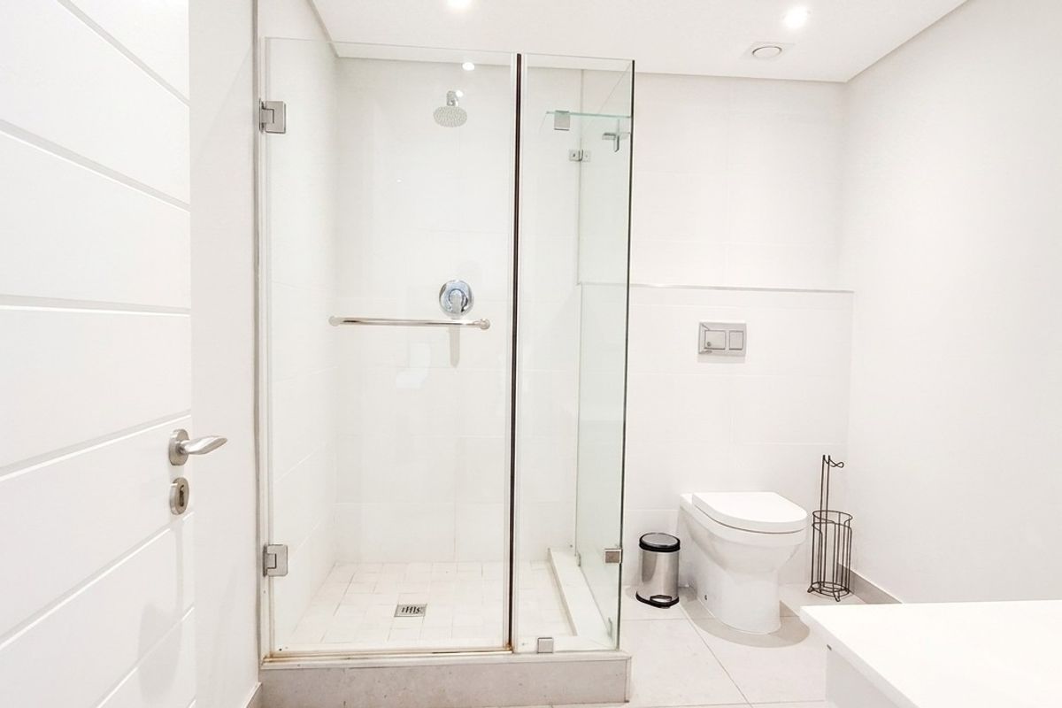 A modern, minimalist bathroom featuring a glass-enclosed shower, wall-mounted toilet with concealed cistern, and clean white finishes throughout.
