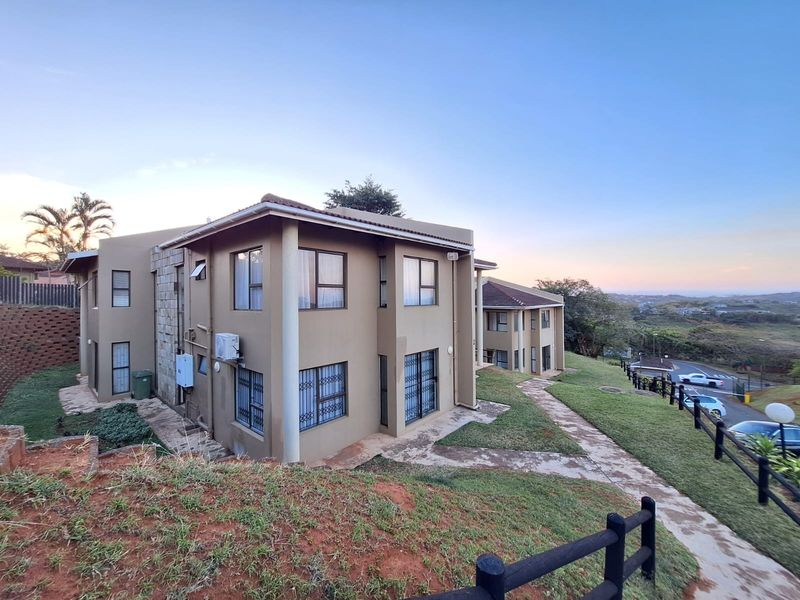 Rear view of a multi-story apartment complex featuring paved walkways, security bars on windows, and landscaped grounds with timber fencing.