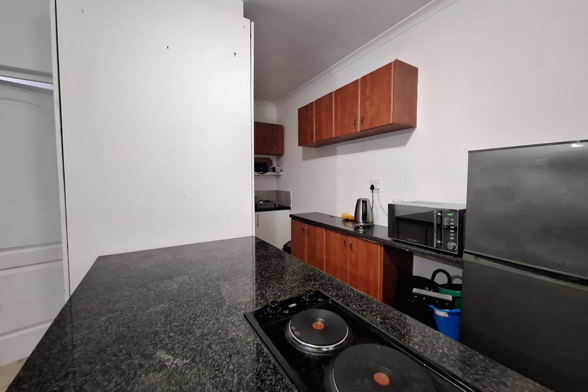 Compact kitchen featuring dark granite countertops, built-in wooden cabinetry, and a fitted electric hob, providing a functional workspace.