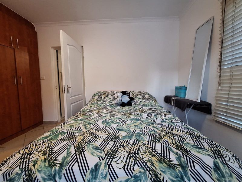 A functional bedroom featuring built-in wooden cupboards, tiled flooring, and venetian blinds, providing a practical and well-lit sleeping space.