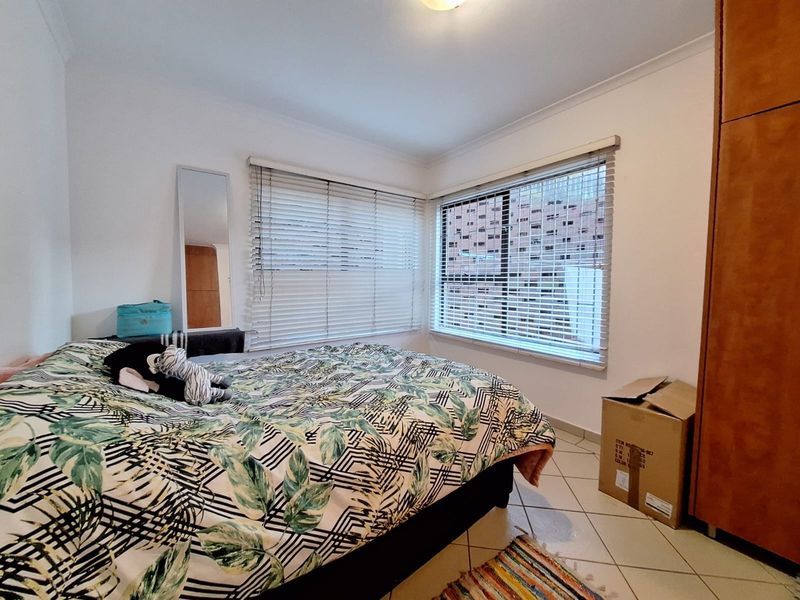 A bedroom featuring tiled flooring, built-in wardrobe storage, and corner windows fitted with venetian blinds.